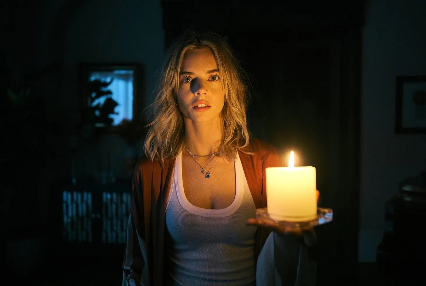 A blonde haired woman (Samara Weaving) in a dark room holding a candle in Borderline.