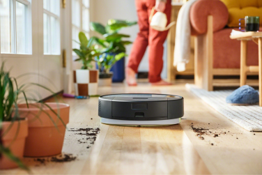 Black Roomba 205 robot vacuum mopping hardwood floor near potted plants