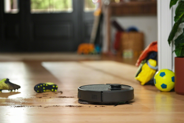 Black Roomba Plus 405 robot vacuum mopping hardwood floor with soccer equipment in background